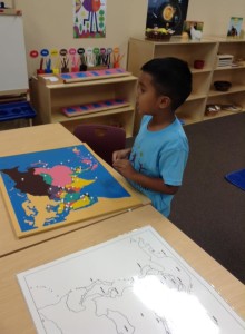 A boy playing with a world map at Lutz Montessori School and Montessori at Trinity Oaks
